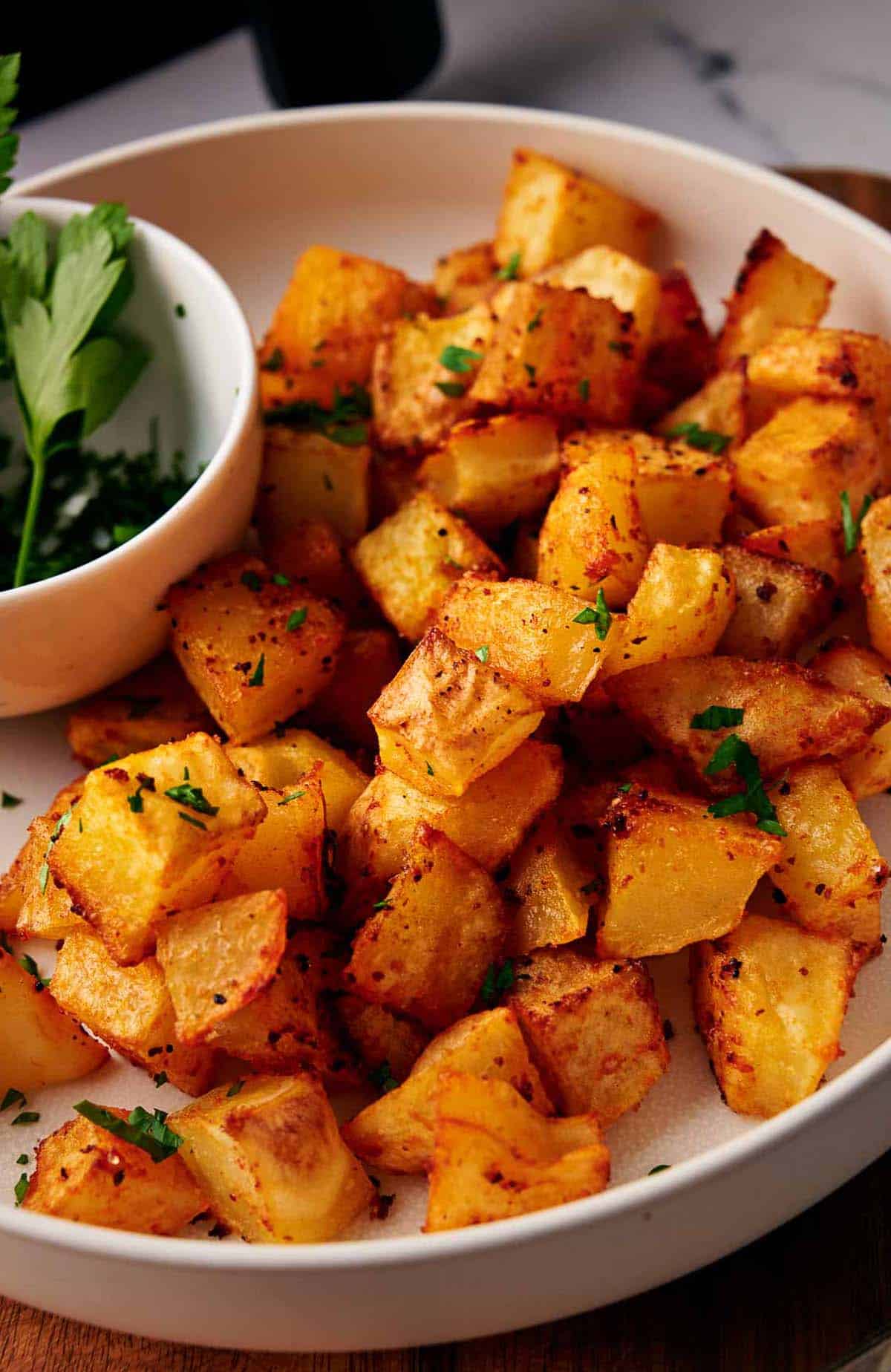 Delicious air fryer breakfast potatoes in a serving bowl along with fresh parsley.
