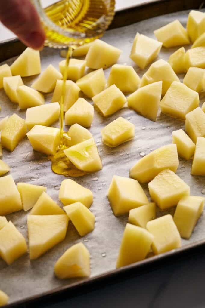 Drizzling olive oil over potato cubes.