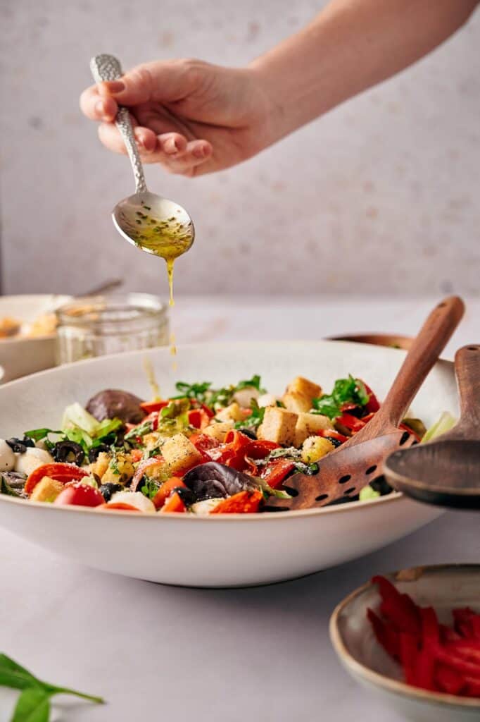 Someone drizzling Italian seasoning over the salad.