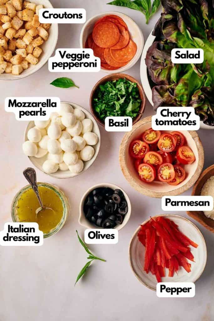 Ingredients needed; crouton, veggie pepperoni, salad, cherry tomatoes, fresh basil, veggie Parmesan, red bell pepper, black olives, Italian seasoning, and Mozzarella pearls.