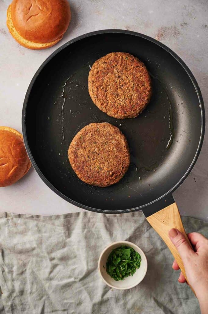 Veggie burgers cooking in a cast iron skillet.