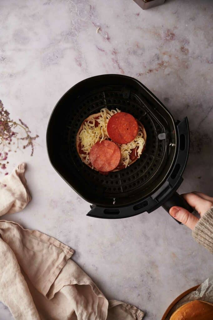 A person is holding a bagel pizza in a pan.