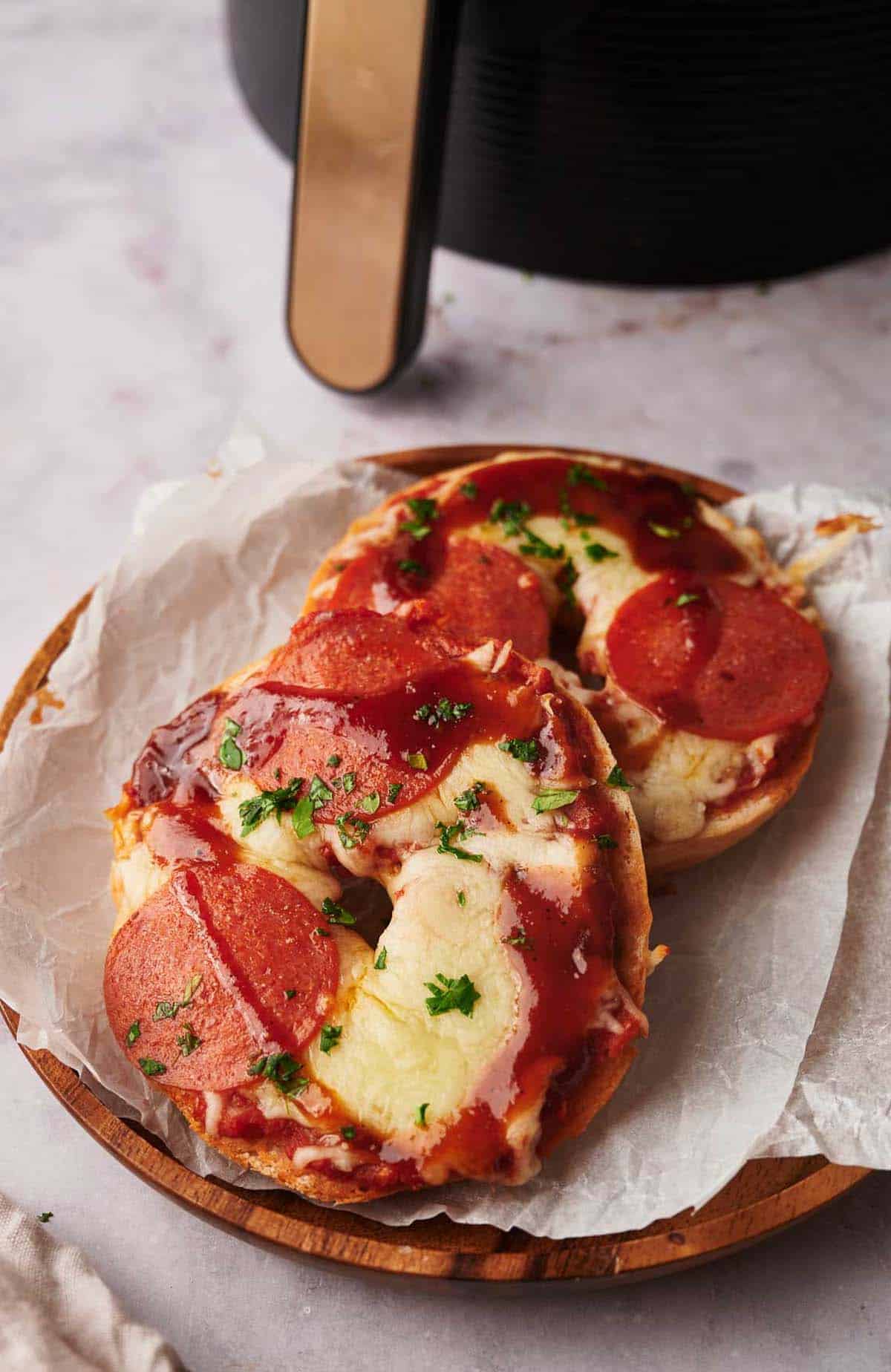 Two pepperoni bagel pizzas on a plate next to an air fryer.