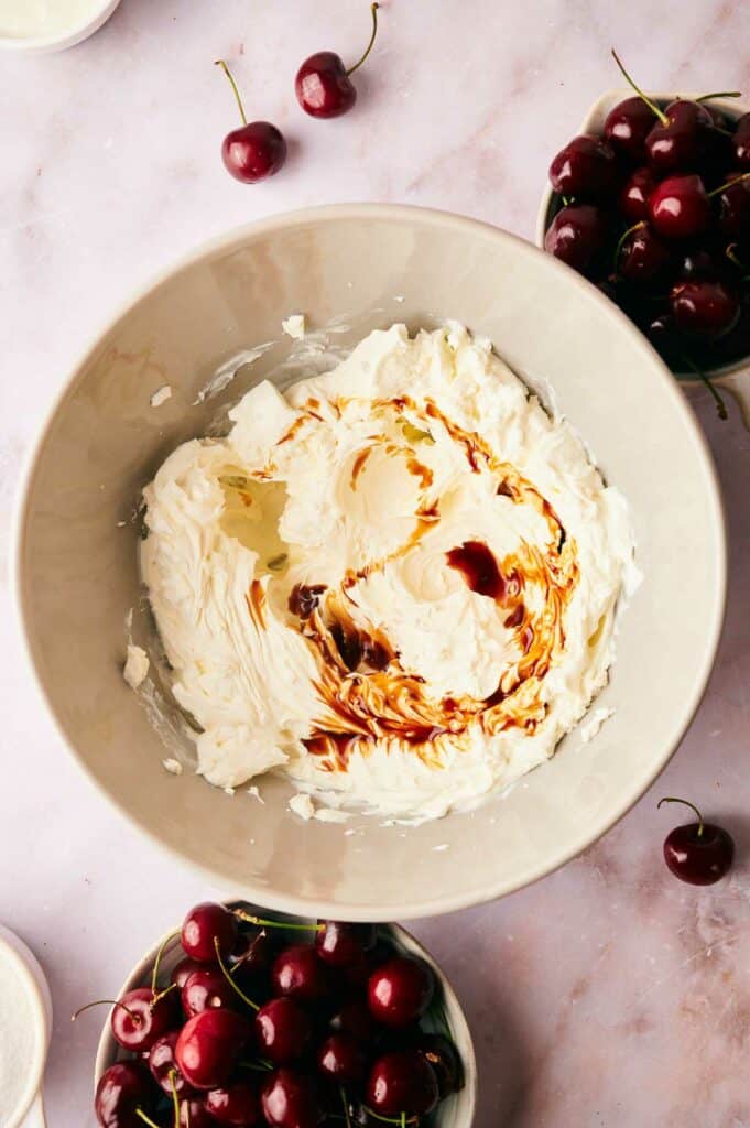 A bowl of whipped cream cheese and vanilla with cherries in a bowl nearby.