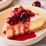 A slice of cheesecake with cherries on a plate.