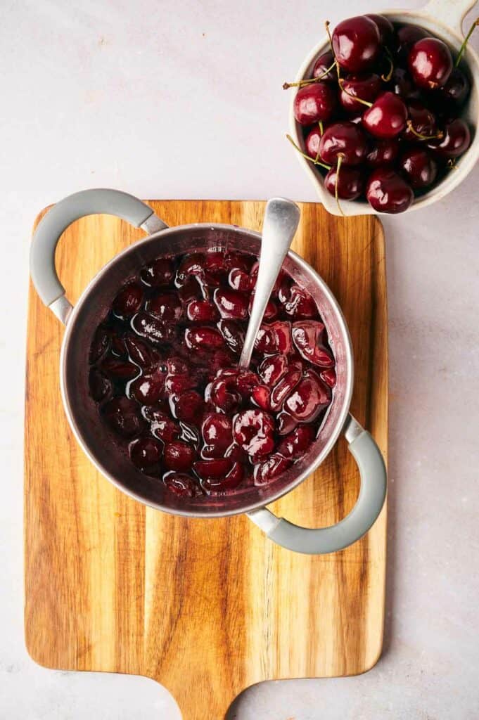 A bowl of cherry sauce on a wooden cutting board.