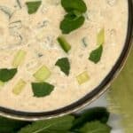 Cucumber raita in a bowl with mint leaves.