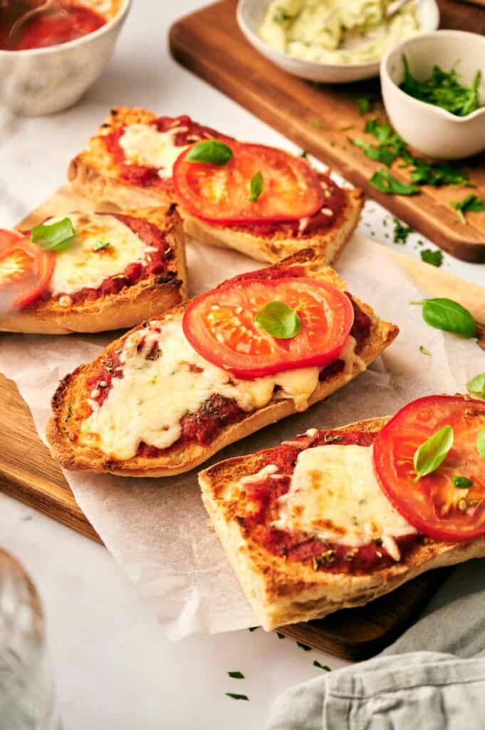 Four slices of French bread pizza with tomatoes and basil on a cutting board.
