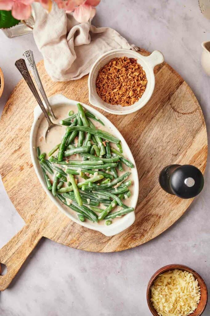 A plate with green beans and other ingredients on a wooden cutting board.