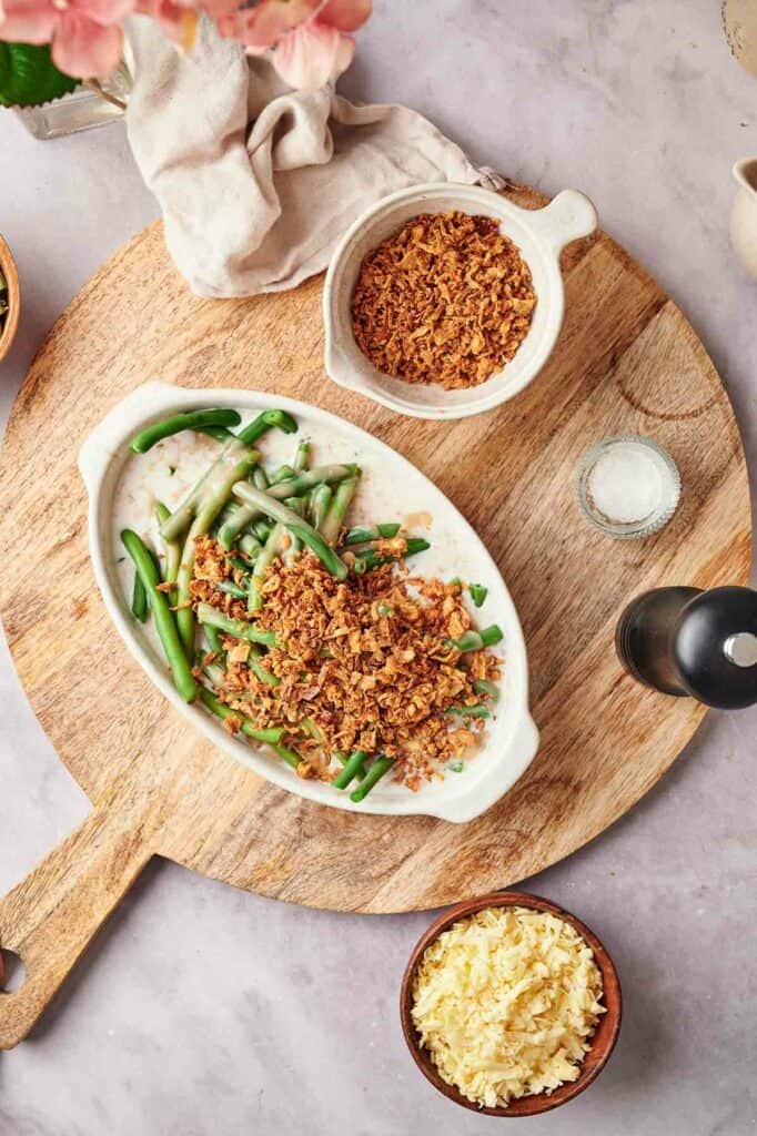 A dish with green beans, cheese and crumbs on a wooden cutting board.