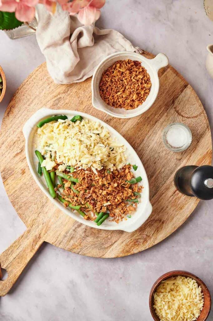 A dish with green beans and cheese on a wooden cutting board.