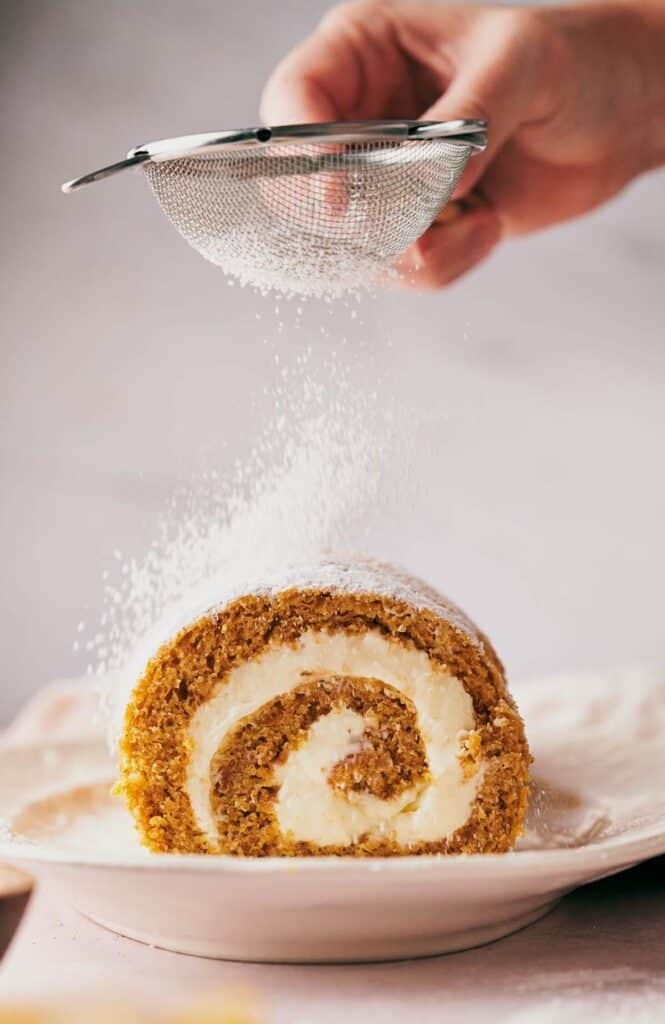 A person is sprinkling sugar on a pumpkin roll.