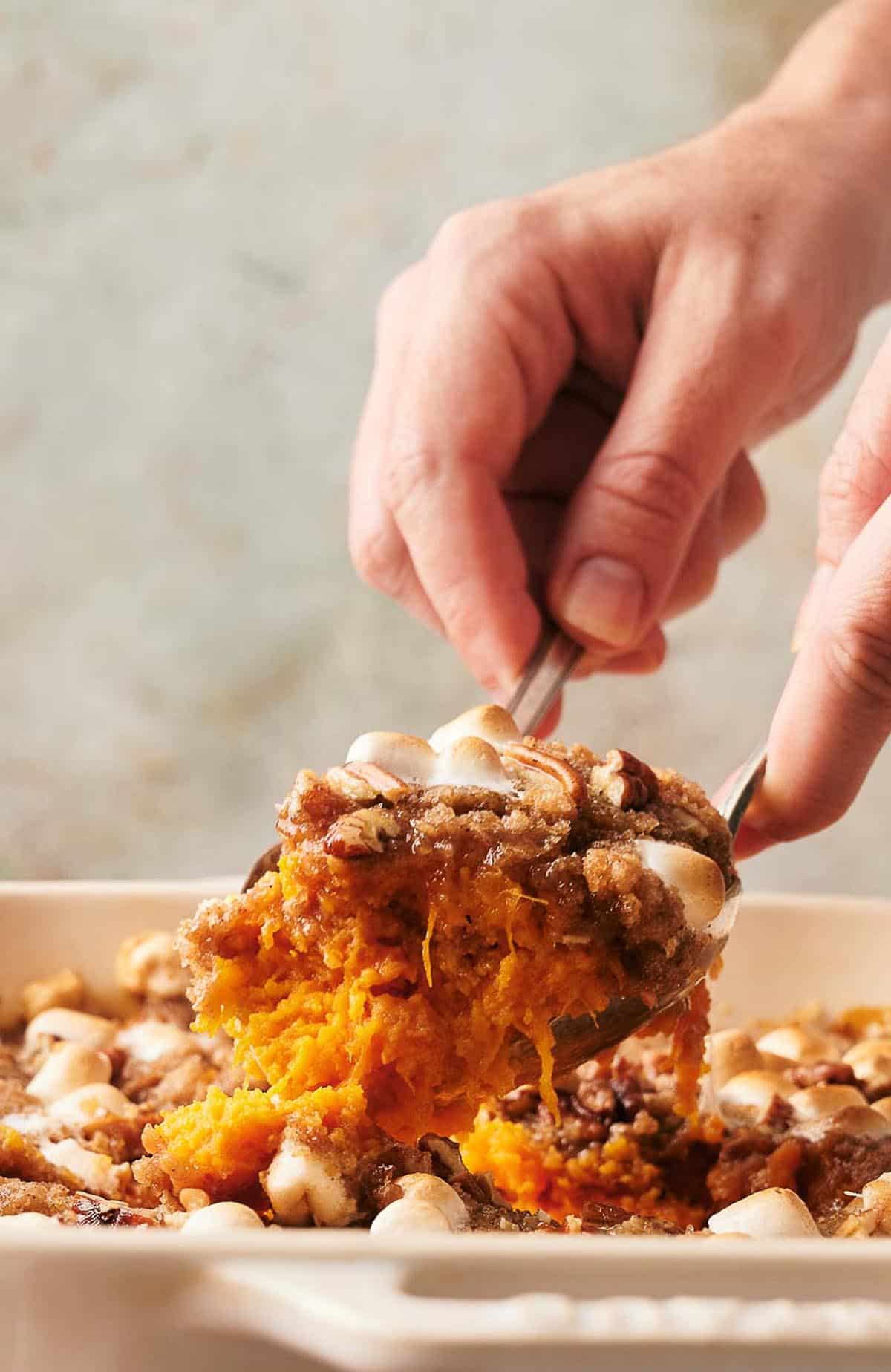 A person scooping a sweet potato casserole out of a dish.