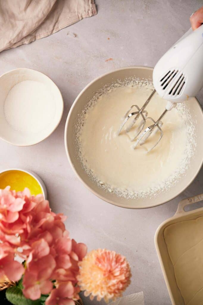 A person using a hand mixer to whisk cream cheese mixture.