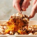 A person is taking a portion of sweet potato casserole.