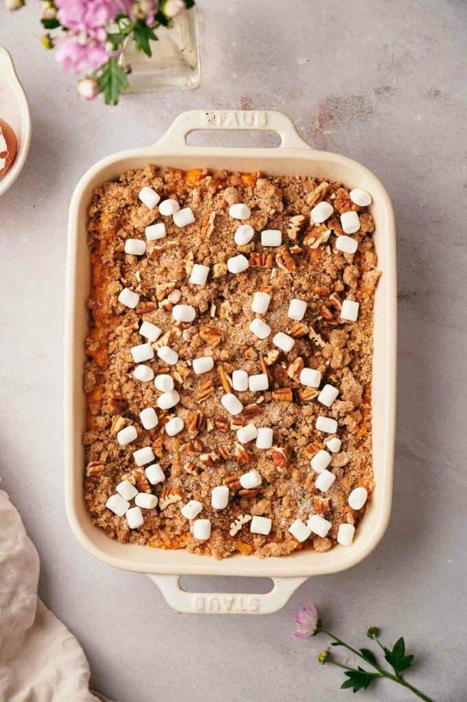 A casserole dish with marshmallows and pecans on it.