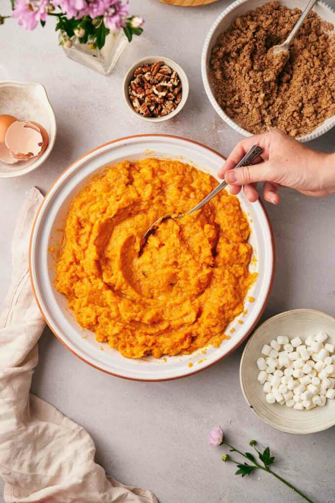 A person is mixing ingredients in a bowl of sweet potato mashed potatoes.