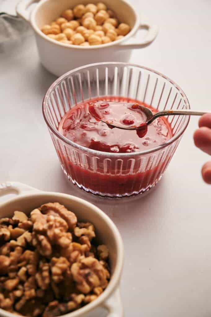 A person is dipping a spoon into a dish with Cranberry sauce and bowl of nuts and a bowl of strawberry sauce.