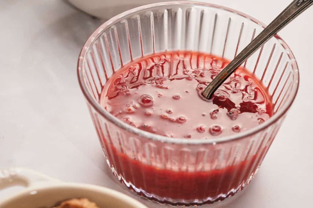 A glass of Cranberry sauce with a spoon next to it.