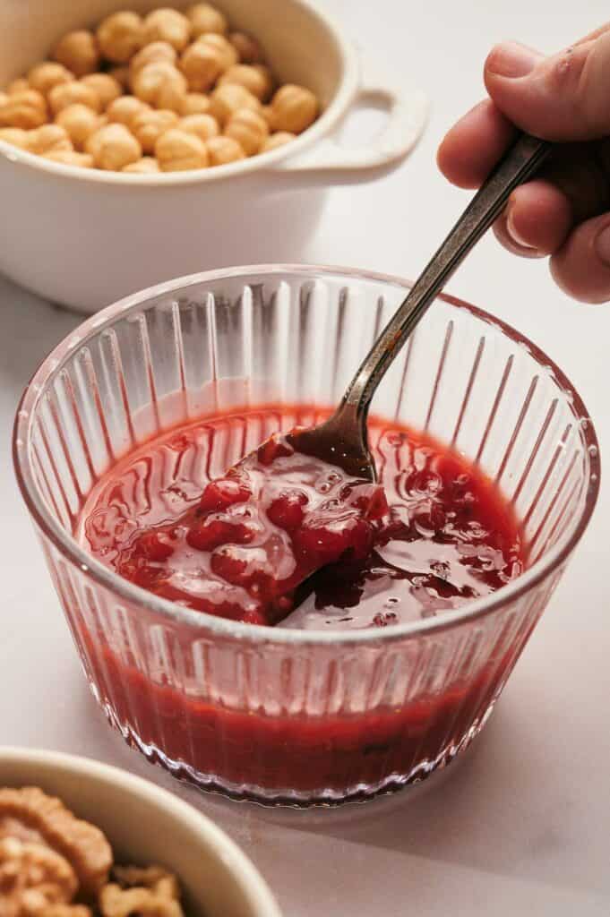A person is dipping a spoon into a bowl of cranberry sauce.