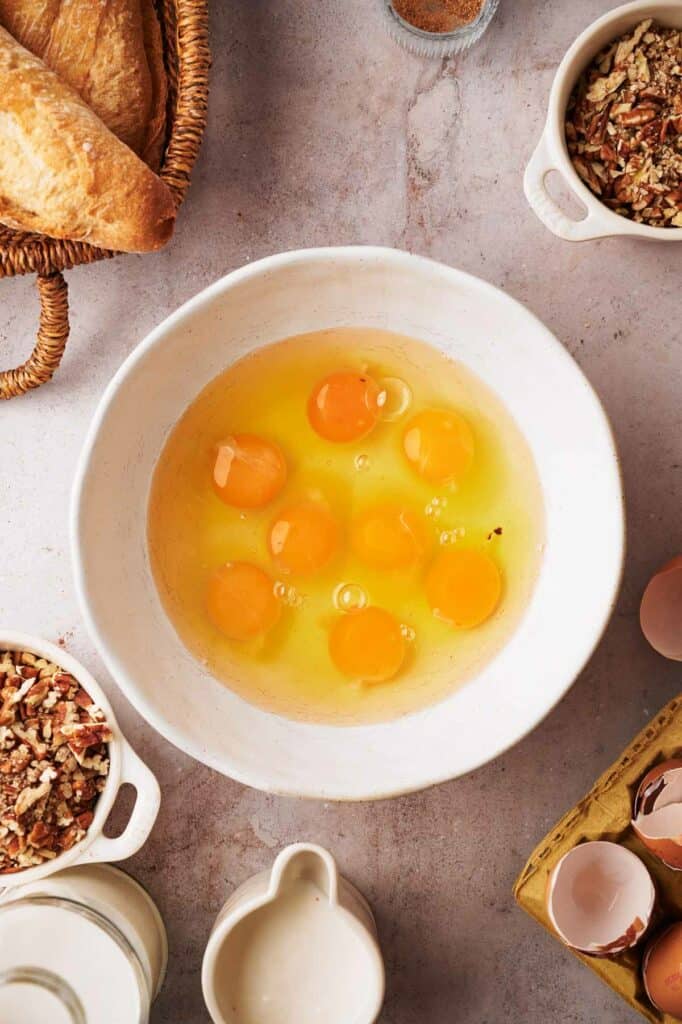 Eggs in a bowl next to bread and other ingredients.
