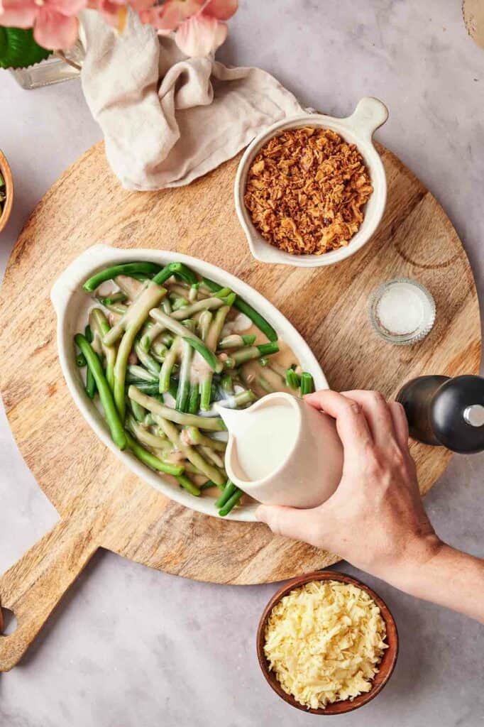 A person pouring milk into a bowl of green beans.