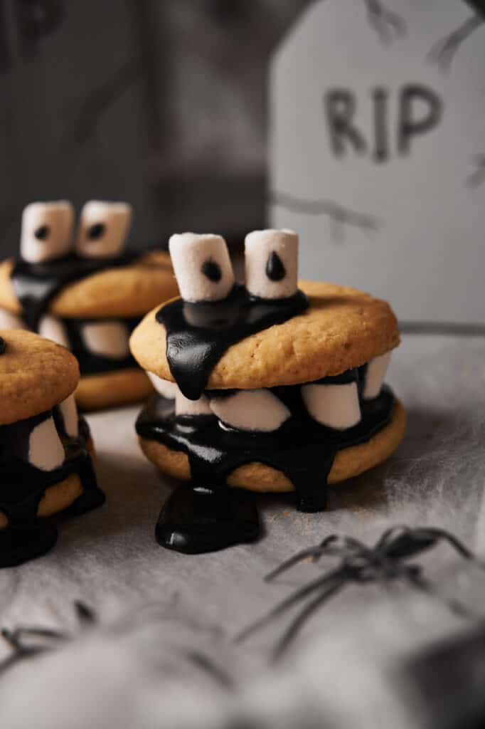 A group of halloween cookies with black frosting and marshmallows.