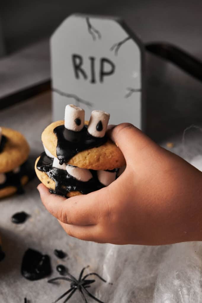 A hand holding a black and white smores sandwich with a tombstone.