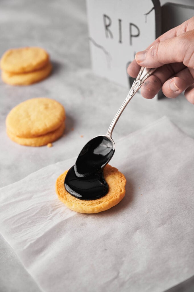 A person is dipping a spoon into a cookie with black icing.