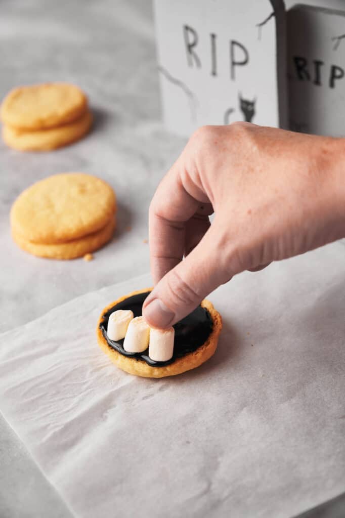 A person is putting marshmallows on a cookie.