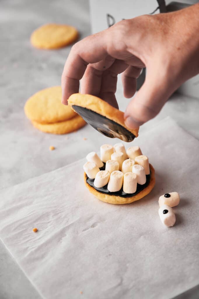 A person is putting the upper layer on a cookie lined with marshamallows.