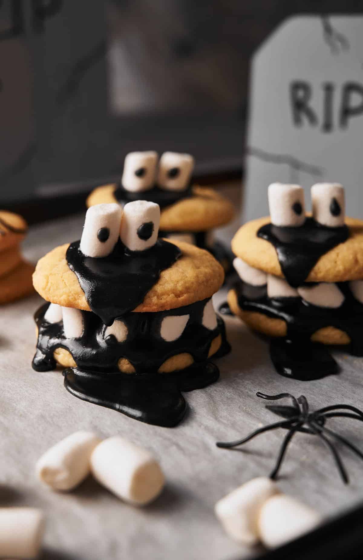 Halloween cookies with black frosting and marshmallows on a baking sheet.