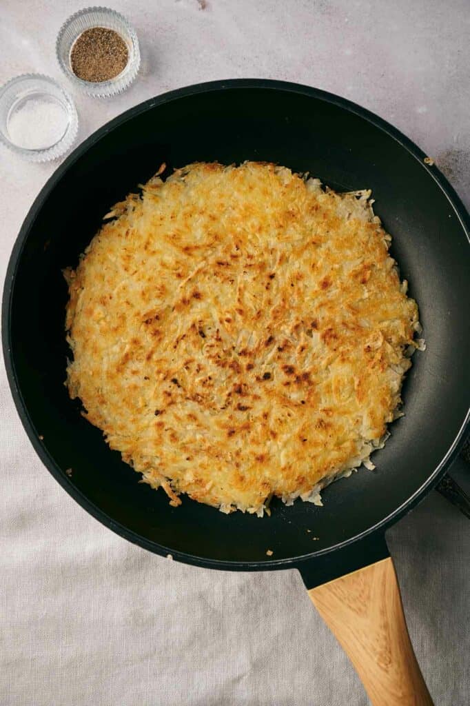 Fried potatoes in a frying pan with a wooden spoon.