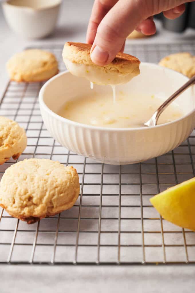 A person dipping lemon cookies into a bowl of lemon glaze.