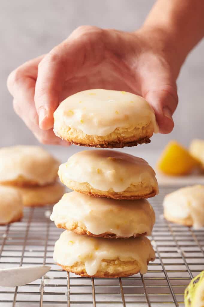 A person holding a stack of lemon cookies on a cooling rack.