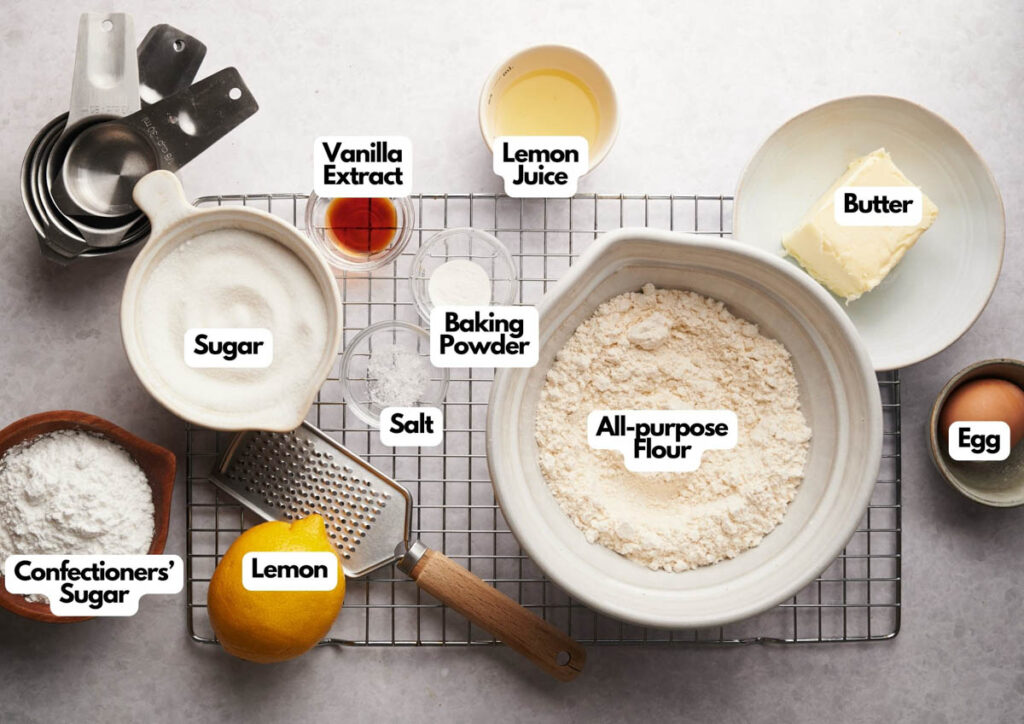 Baking ingredients for spooky Halloween cookies&mdash;including all-purpose flour, sugar, butter, egg, lemon juice, and vanilla extract&mdash;are arranged on the countertop, ready to create festive treats.
