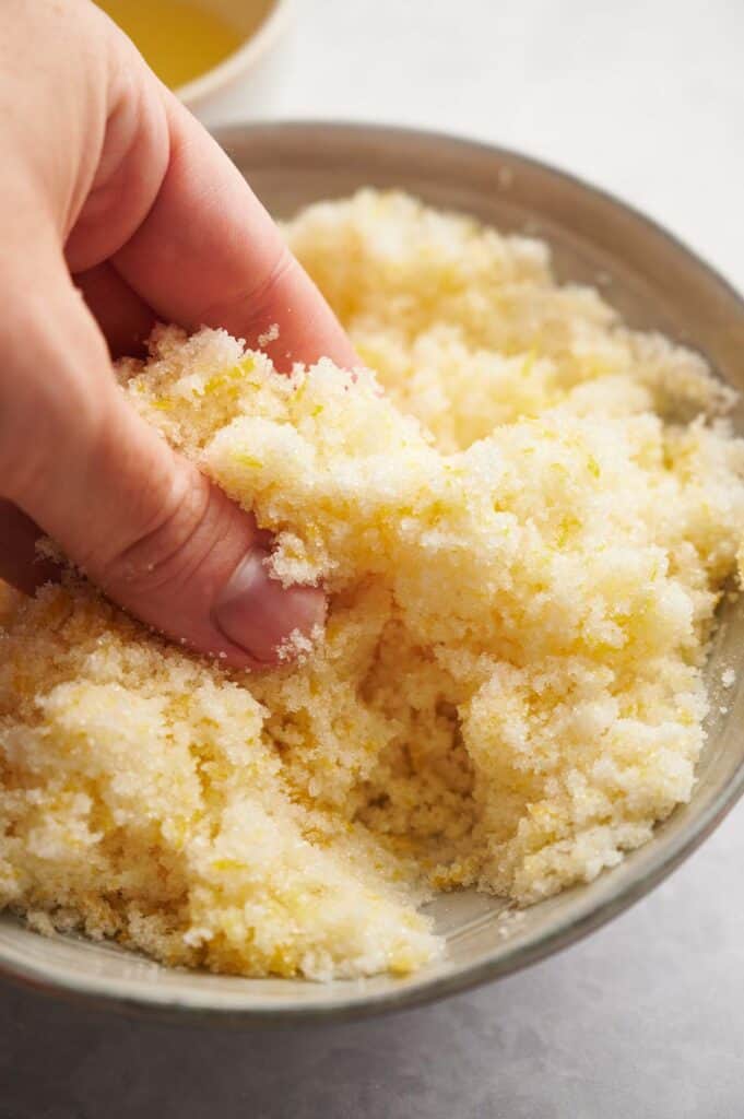 A hand is rubbing lemon zest and sugar together.