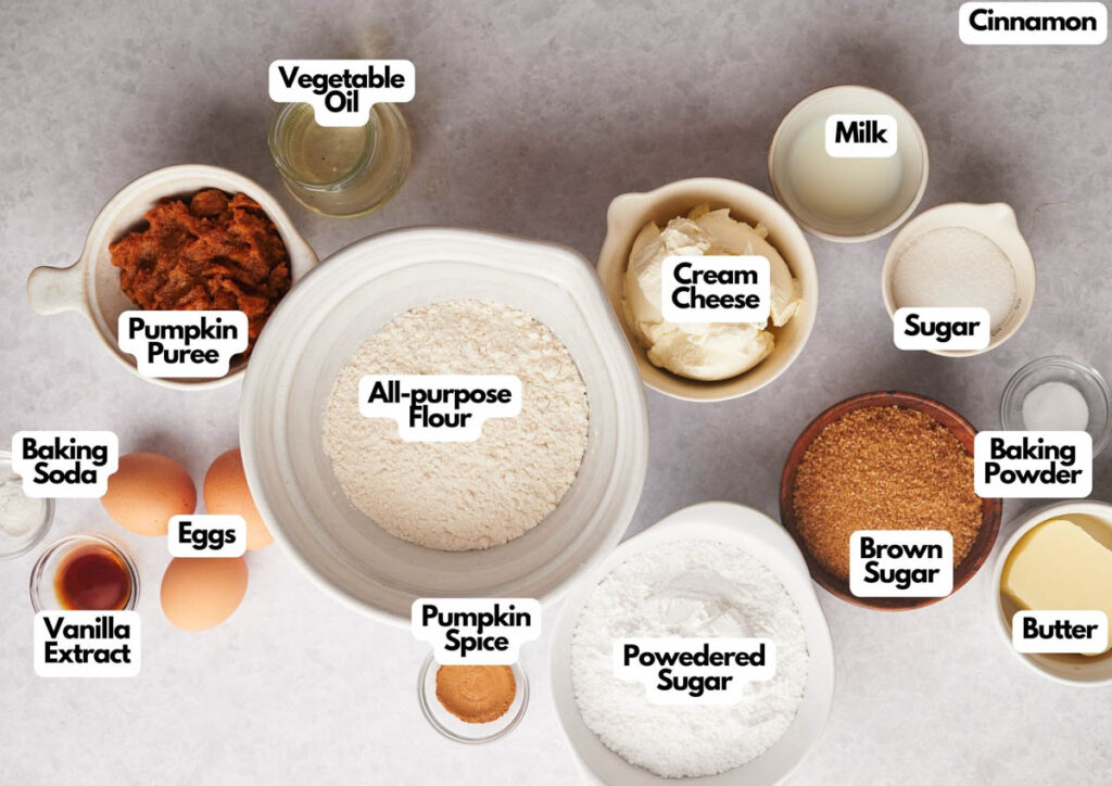 Various baking ingredients in bowls and jars are labeled, including all-purpose flour, pumpkin puree, cream cheese, eggs, sugar, brown sugar, spices, baking soda, baking powder, and butter&mdash;everything you need for spooky Halloween cookies.