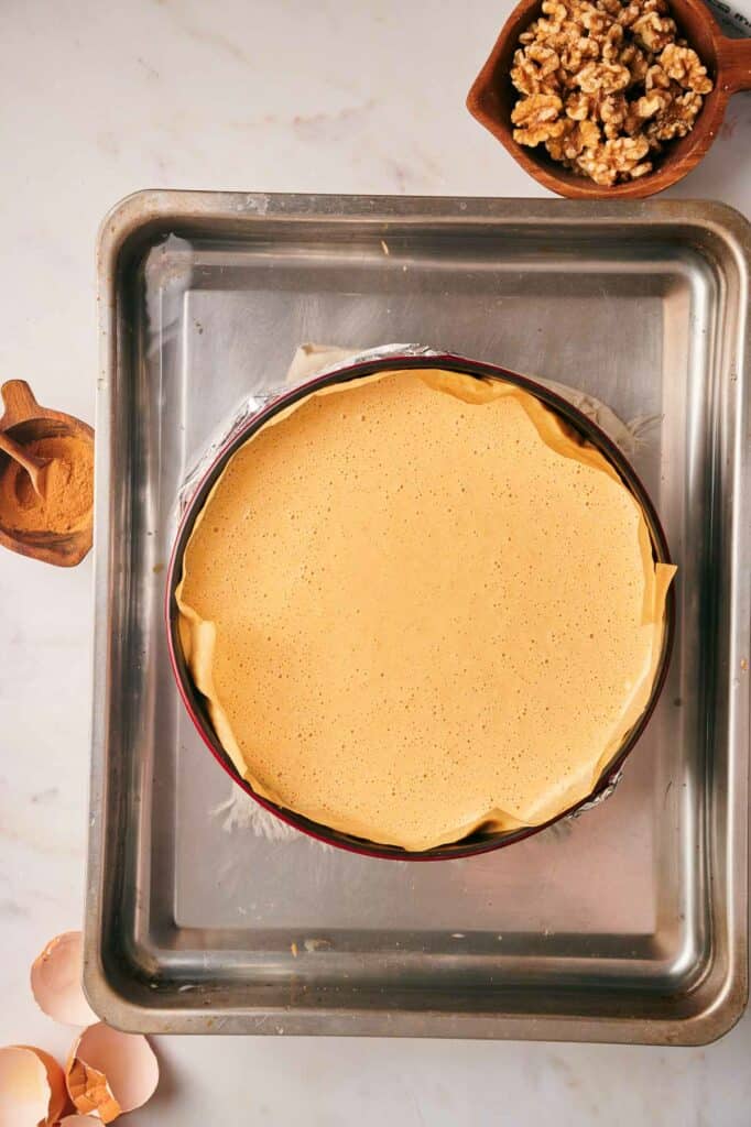 An uncooked pumpkin pie on a baking sheet with nuts on top.