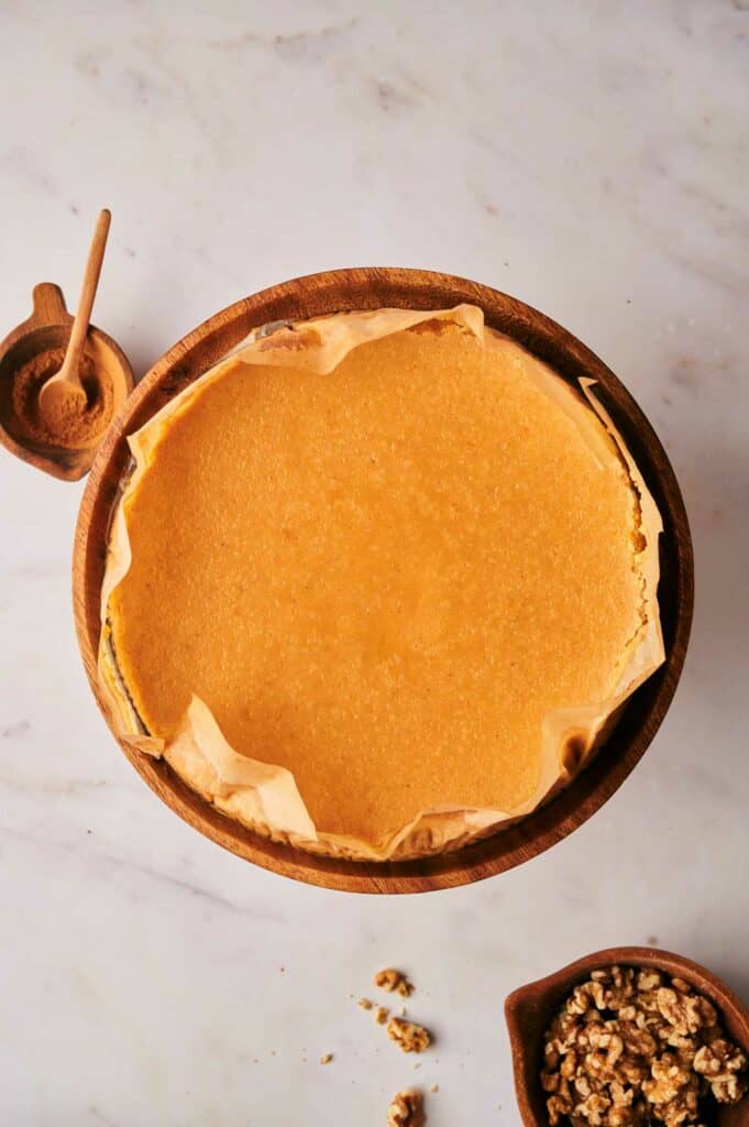 A pumpkin pie is sitting on a table next to a bowl of nuts.