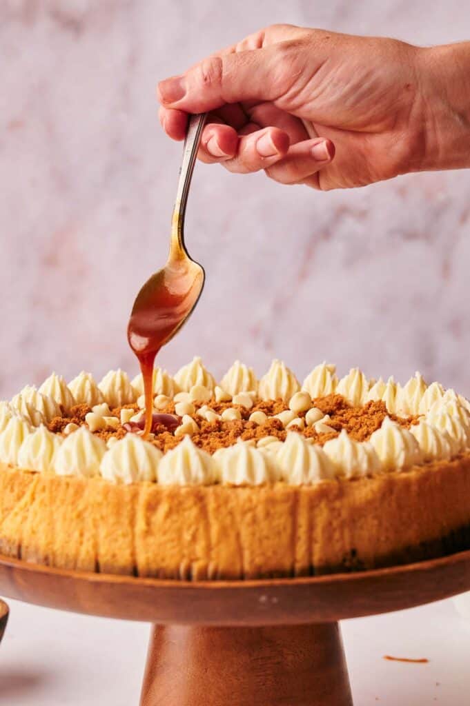 A person drizzling caramel sauce on a cheesecake.
