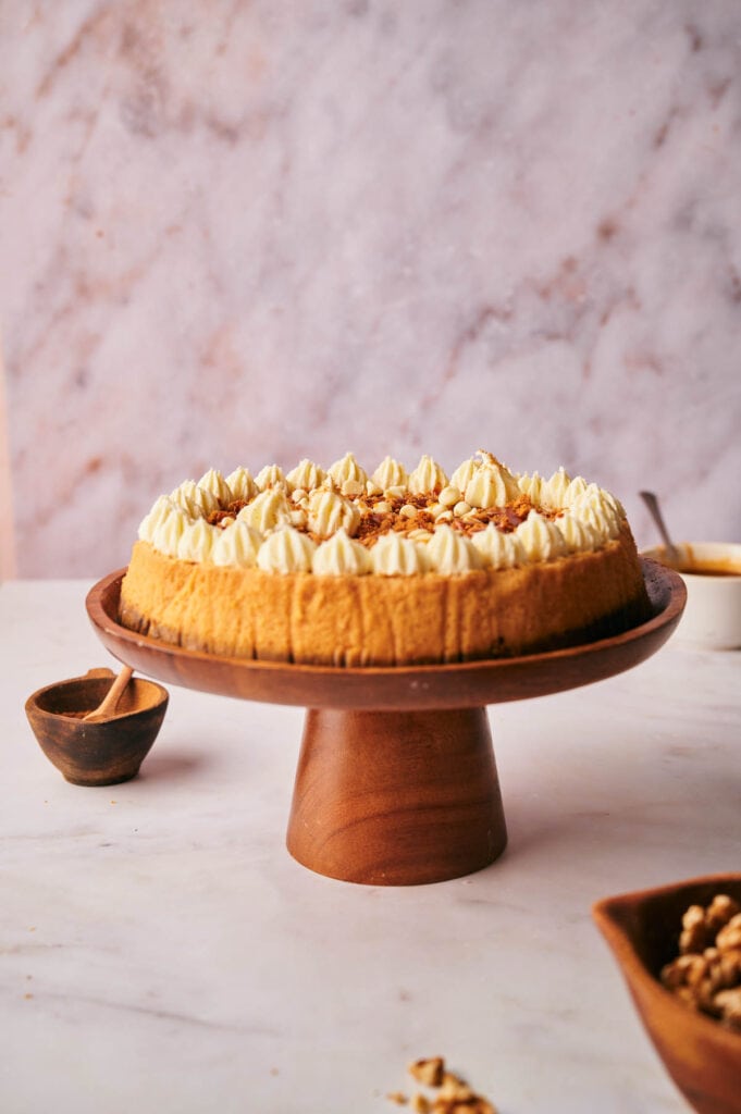 A pumkin pie cheesecake on a wooden stand with whipped cream and nuts on it.