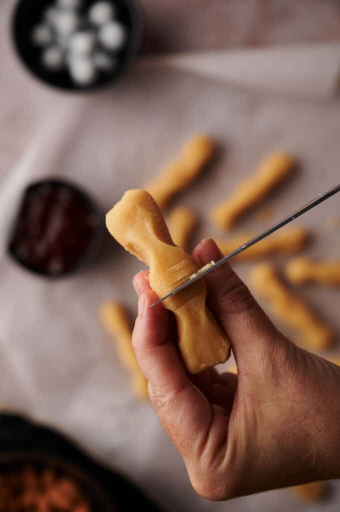 A person using a knife to cut knuckles into cookie dough finger.