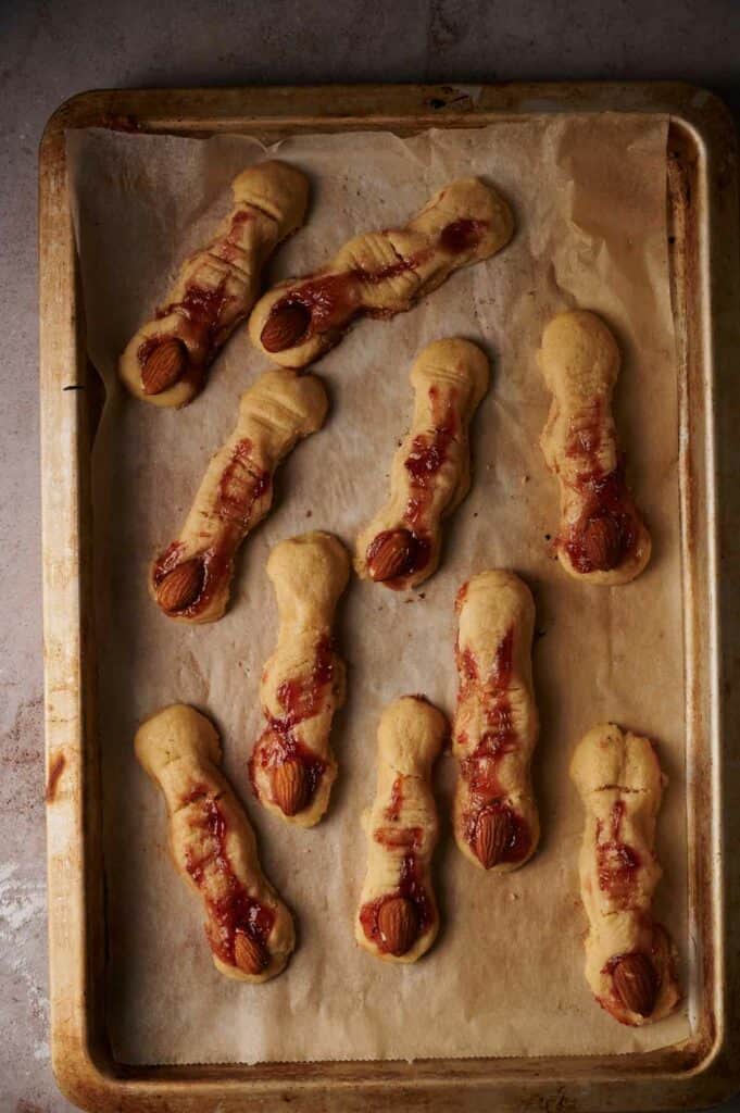 A baking sheet with a tray of baked witch fingers on it.