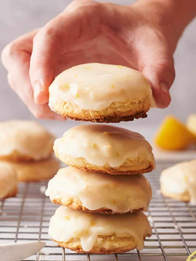 A person holding a stack of lemon cookies on a cooling rack.