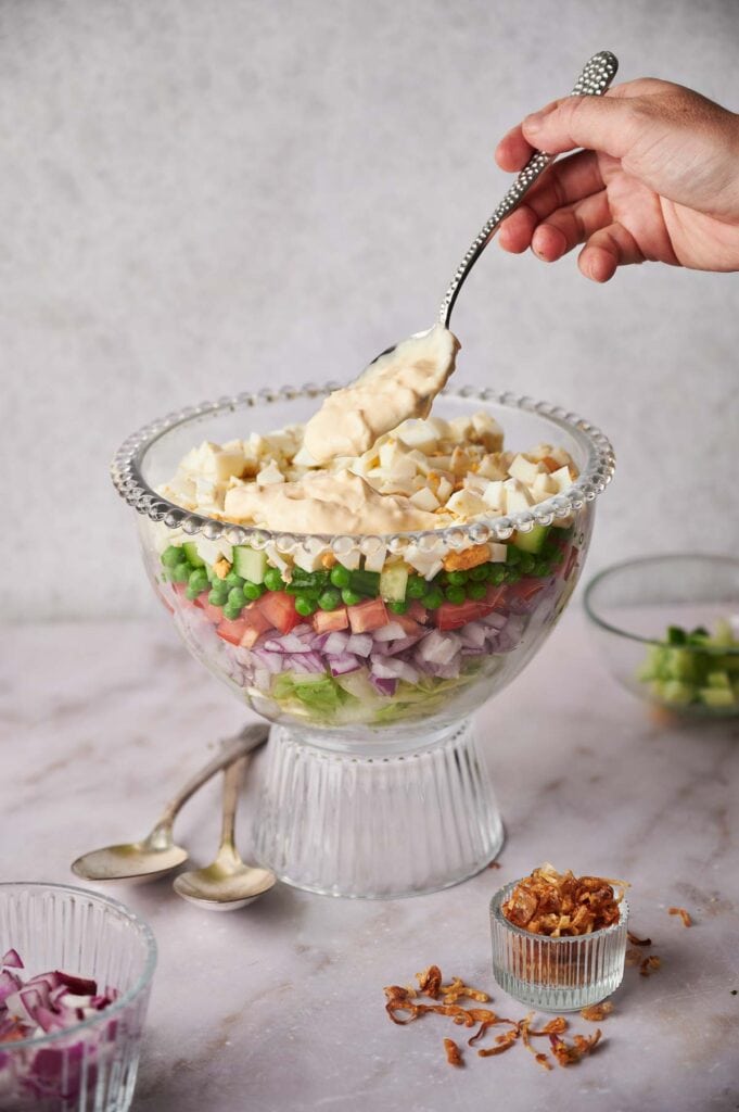 A person is pouring a spoonful of dressing onto a bowl of salad.