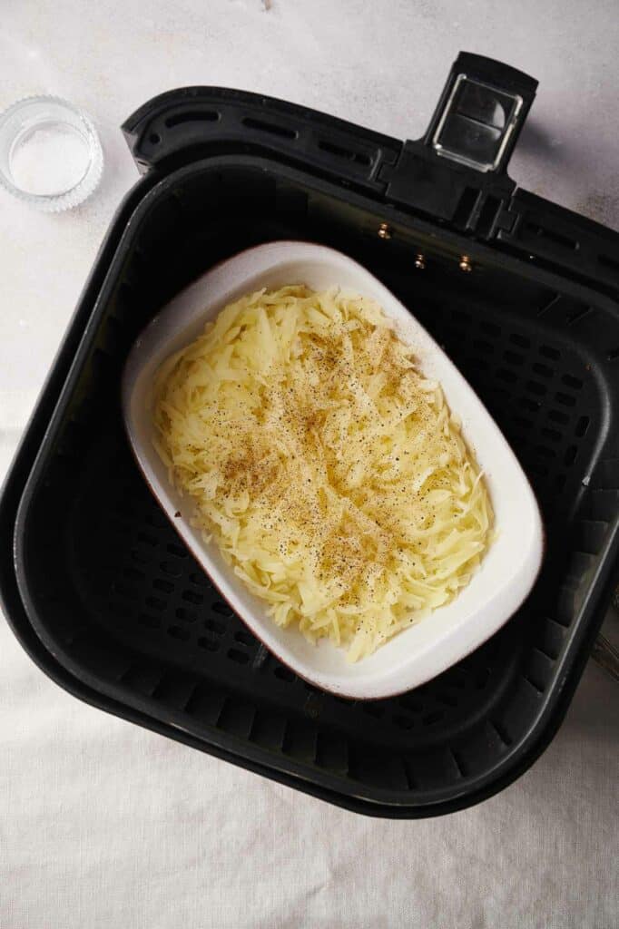 A dish of shredded potatoes in an air fryer.