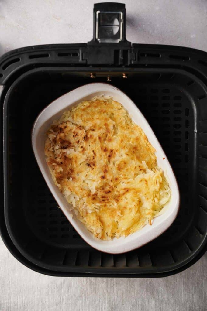 An air fryer with a dish of homemade hash browns in it.