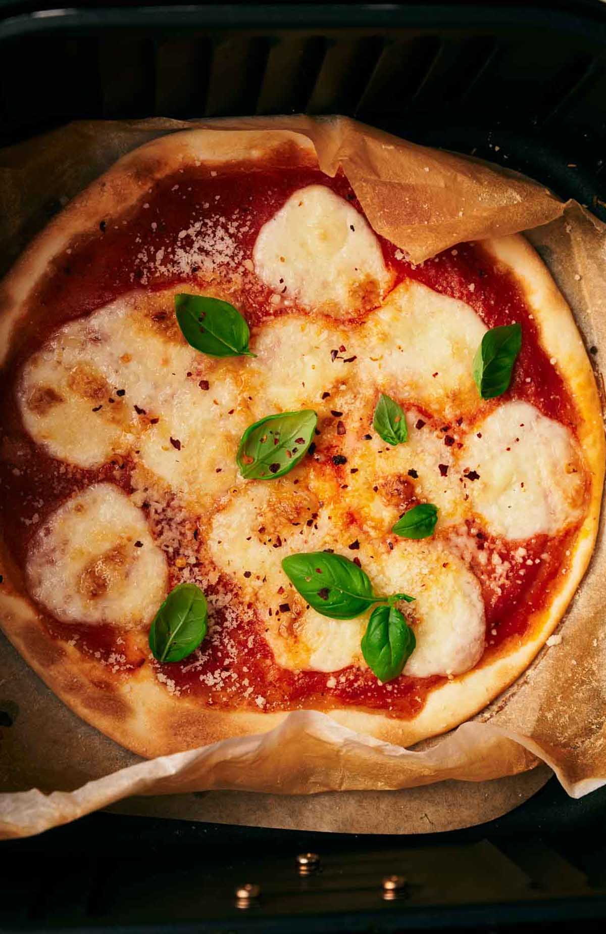 A pizza in an oven with basil leaves on it.