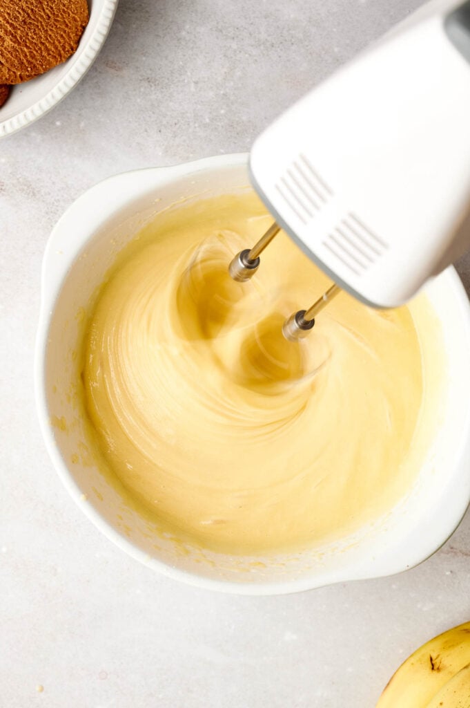 Silky vanilla pudding mixture being whisked smooth in a white mixing bowl with a hand mixer